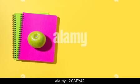 Bannière avec fournitures scolaires, carnets, pomme verte sur fond jaune. Vue de dessus avec espace de copie. Banque D'Images
