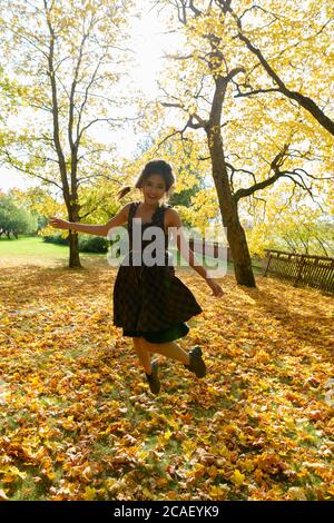 Jeune femme asiatique heureuse souriant en sautant dans des feuilles d'automne pittoresques et des arbres dans la forêt Banque D'Images