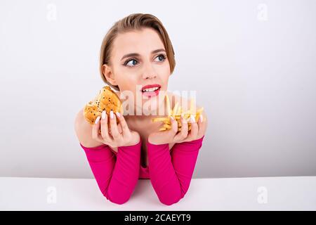 la fille tient des frites et un hamburger dans ses mains, des vêtements roses et un maquillage brillant, des cheveux blancs courts, des aliments rapides délicieux, une fille de hamburger Banque D'Images