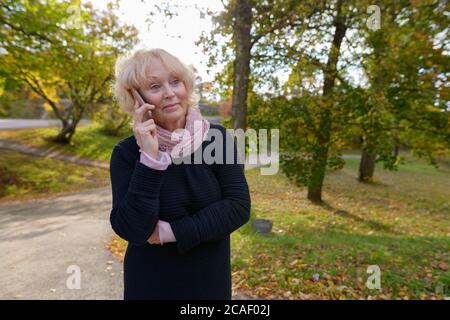 Femme sénior et attentionnés parlant sur un téléphone portable sur le chemin d'un parc naturel calme et reposant Banque D'Images