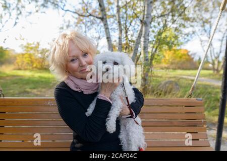 Femme âgée tenant son chien tout en étant assise sur un banc en bois avec vue panoramique naturelle sur le parc Banque D'Images