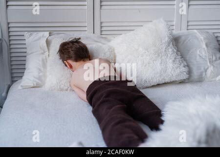 l'enfant est offensé, se trouve sur un lit blanc, son visage dans un oreiller, triste humeur , Banque D'Images