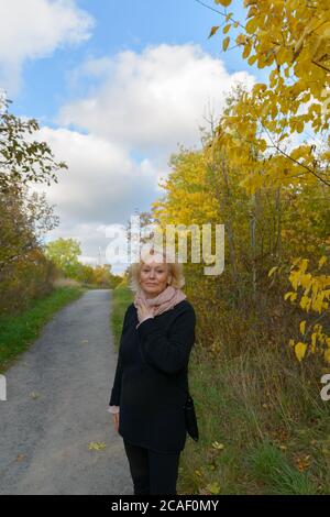 Femme âgée portant un foulard sur un sentier avec de jeunes arbres d'automne dans le parc Banque D'Images