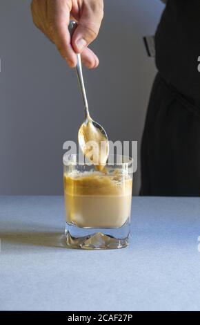 Dose verticale d'une personne remuant le café avec une cuillère dans une tasse transparente sur une surface blanche Banque D'Images