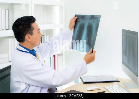Homme asiatique médecin tenant et cherchant à examiner les rayons X des poumons et du cerveau du patient dans une clinique médicale à l'hôpital. Banque D'Images