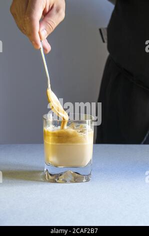 Un cliché vertical d'une personne remuant du café avec une cuillère dans une tasse transparente sur une surface blanche Banque D'Images