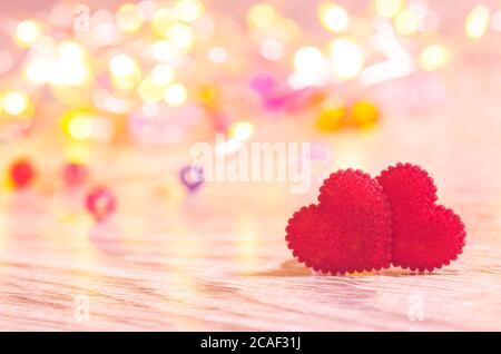 Gros plan de deux coeurs rouges sur une table en bois contre des lumières de bokeh diffurées. Banque D'Images