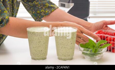 Smoothie de banane de céleri aux graines de Chia et au miel en verres, servi avec des framboises fraîches et des feuilles de menthe, en gros plan sur une table de cuisine. Breakfa sain Banque D'Images