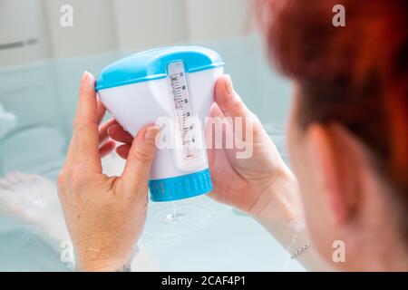 Femme à tête rousse dans un bain à remous contrôlant la température de l'eau Banque D'Images