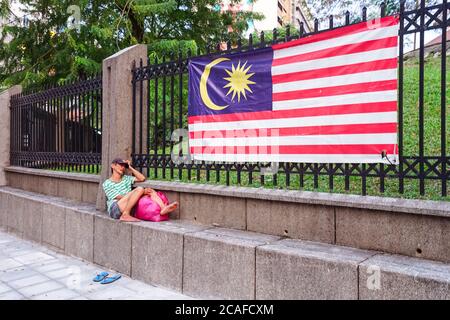 Kuala Lumpur / Malaisie - 14 février 2019 : homme sans domicile allongé sur un mur avec drapeau malaisien accroché à des barres Banque D'Images