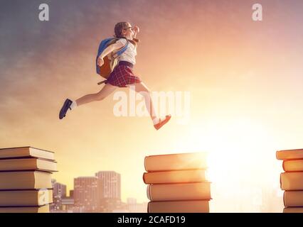 Retour à l'école! Heureux mignon enfant industriel courir et sauter sur des livres sur fond de coucher de soleil paysage urbain. Concept d'éducation et de lecture. T Banque D'Images