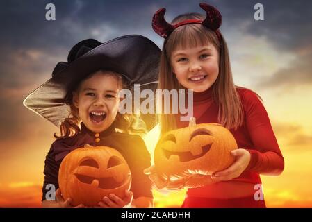 Deux sœurs heureuses pour Halloween. Enfants amusants en costumes de carnaval en plein air. Enfants et citrouilles gais sur fond de coucher de soleil. Banque D'Images