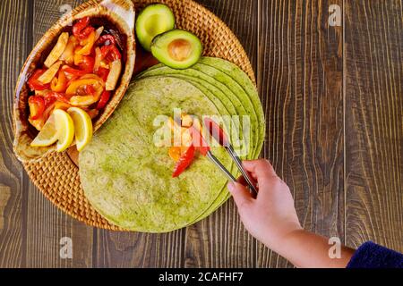 La femme met des légumes frits et de la viande sur des tortillas aux épinards verts. Banque D'Images