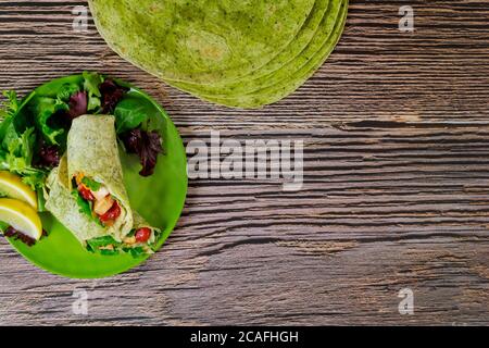 Envelopper de poulet grillé et de légumes sur des tortillas vertes aux épinards sur une table en bois. Banque D'Images