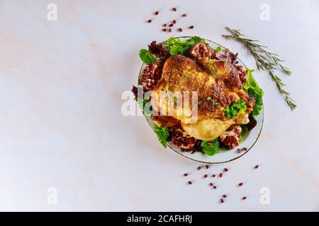 Poulet entier grillé sur une assiette avec salade verte et grenade sur fond blanc. Banque D'Images