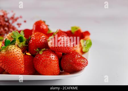 Fraises fraîches bio avec fleurs sur plaque sur fond blanc. Banque D'Images