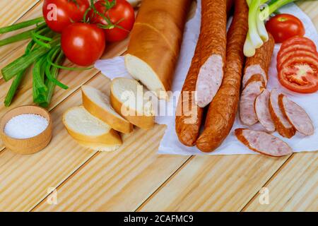 Saucisses Krakowska sur papier avec légumes et sel sur table en bois. Banque D'Images