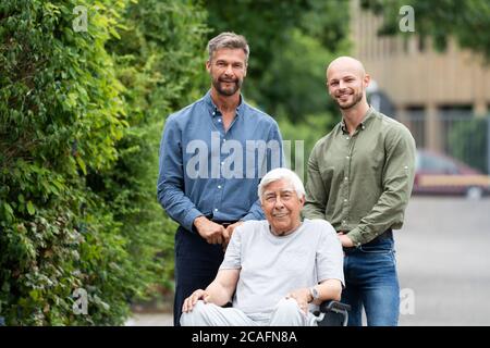 Grand-père handicapé en fauteuil roulant avec famille de soins Banque D'Images