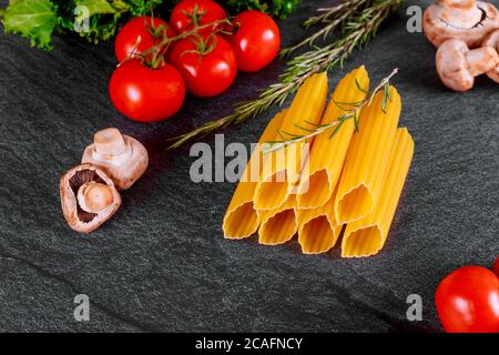 Séchez les pâtes de manucotti avec les champignons et la tomate sur fond noir. Banque D'Images