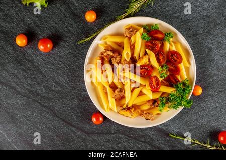 Pâtes Penne avec tomates cerises coupées en deux et viande sur fond noir. Banque D'Images