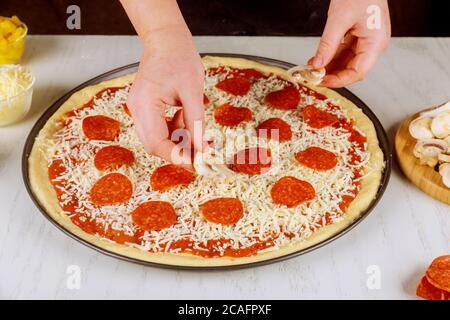 Femme mettant des champignons tranchés sur de la pâte à pizza crue. Banque D'Images
