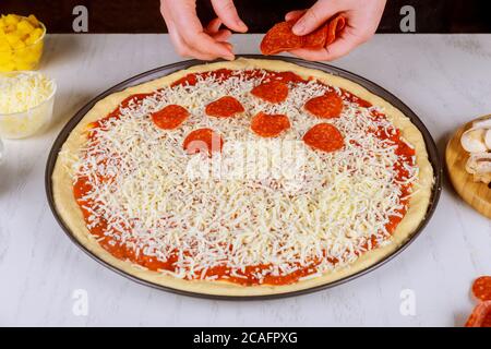 Femme mettant des tranches de pepperoni sur de la pâte à pizza crue. Banque D'Images