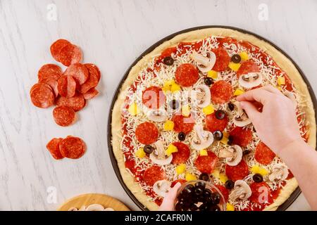 Femme mettant des tranches d'olives sur de la pâte à pizza crue. Banque D'Images