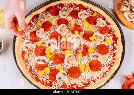 Femme mettant de l'ananas haché sur de la pâte à pizza crue. Banque D'Images
