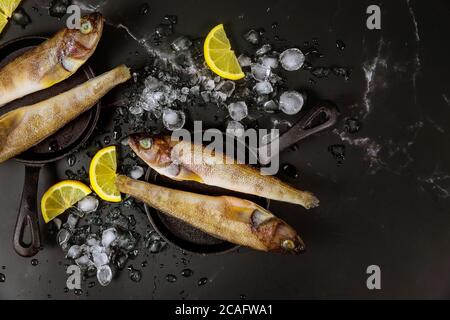 Poisson entier non cuit avec glace et citron sur table noire. Vue de dessus. Banque D'Images