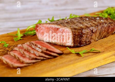 Tranchez le sirloin de bœuf rare moyen avec de l'arugula sur une planche en bois. Banque D'Images