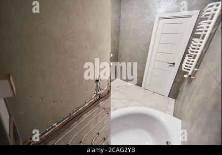 Salle de bains moderne avec sol en marbre et porte blanche avant et après rénovation. Comparaison de l'ancienne salle de bain avec les tuyaux de chauffage au sol et la nouvelle salle de bains avec porte-serviettes chauffant et baignoire. Banque D'Images