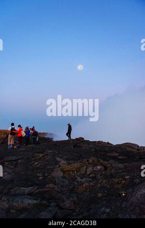 Silhouettes de personnes assises au bord du cratère du volcan Erta Ale, en Éthiopie, en pleine lune Banque D'Images