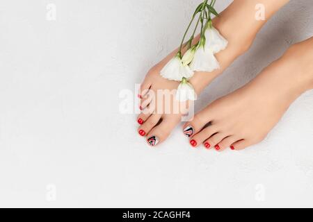 Manucure, pédicure concept de salon de beauté. Pieds de l'utérus sur fond gris. Magnifique motif à ongles rouge d'été. Banque D'Images