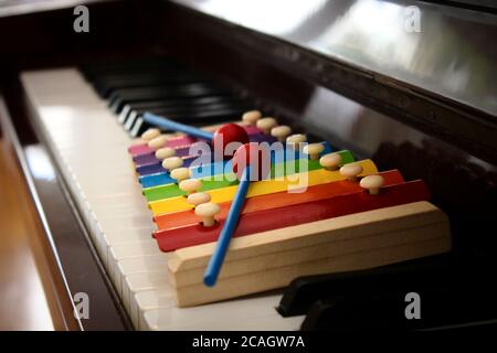 Gros plan d'un jouet xylophone coloré avec des maillets mis sur le clavier d'un piano classique. Banque D'Images