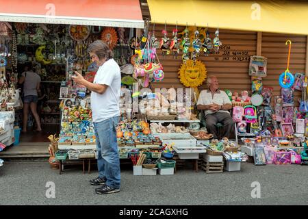 08.08.2018, Tindari, Sicile, Italie - UN commerçant se trouve en face d'une boutique de souvenirs et attend les clients. Marionnettes siciliennes traditionnelles, jouets en plastique Banque D'Images