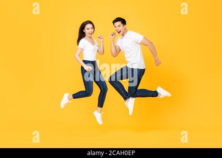 Portrait complet d'un couple asiatique charmant souriant et sautant en milieu d'air isolé sur fond jaune Banque D'Images