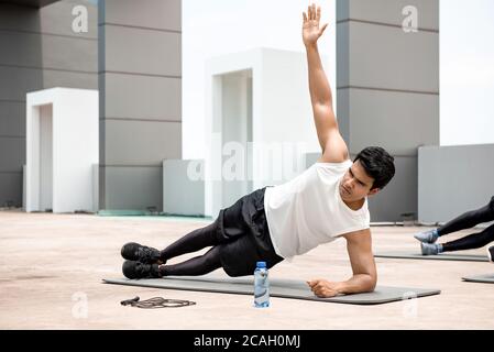 Homme indien athlétique faisant de l'exercice de planche latérale à l'extérieur sur le toit avec des amis Banque D'Images