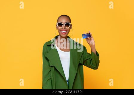 Portrait d'une jeune femme afro-américaine à la mode souriante carte de crédit dans un studio isolé de fond jaune Banque D'Images