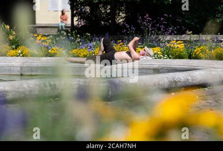 Munich, Allemagne. 07e août 2020. Un homme se trouve au soleil à la fontaine de Neptune, dans le vieux jardin botanique. Credit: Sven Hoppe/dpa/Alay Live News Banque D'Images