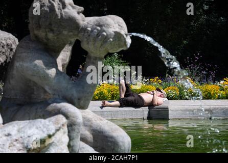 Munich, Allemagne. 07e août 2020. Un homme se trouve au soleil à la fontaine de Neptune, dans le vieux jardin botanique. Credit: Sven Hoppe/dpa/Alay Live News Banque D'Images