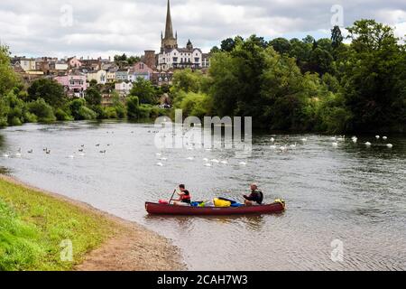 Deux hommes pagayent un canoë par le club d'aviron sur la rivière Wye avec vue sur la ville au-delà. Ross on Wye, Herefordshire, Angleterre, Royaume-Uni, Grande-Bretagne Banque D'Images