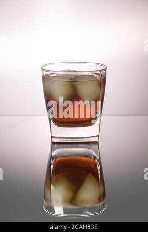 Verre de whisky avec morceaux de glace sur la table miroir. Image verticale avec espace de copie. Banque D'Images