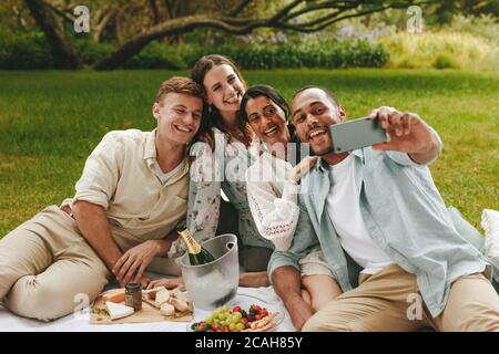 Jeune homme prenant le selfie avec des amis au pique-nique. Groupe multiethnique de jeunes hommes et femmes posant pour un selfie au parc. Banque D'Images