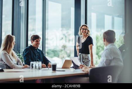 Collègues de bureau ayant une discussion informelle pendant la réunion dans la salle de conférence. Groupe d'hommes et de femmes assis dans la salle de conférence et souriant. Banque D'Images