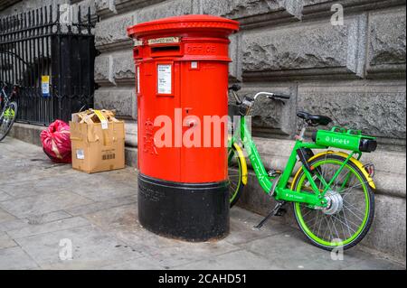 LONDRES - 04 FÉVRIER 2020 : un vélo de location d'assistance électrique Lime stationné entre un mur et une boîte postale britannique rouge traditionnelle avec des ordures jetées Banque D'Images