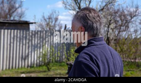 Vue rapprochée depuis l'arrière d'un homme de 60 ans, qui se tient dans le jardin. . Photo de haute qualité Banque D'Images