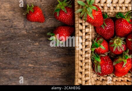 Fraises Juteuses frais dans le panier. Panier en osier plein de fraises fraîchement cueillies sur fond de bois vintage. Temps pour manger des fraises. Banque D'Images