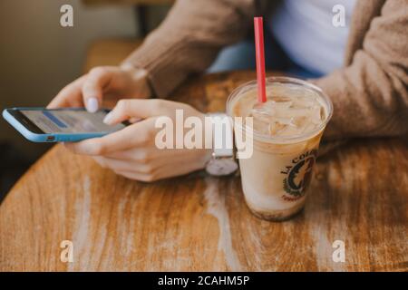 Une fille au brunch de la ville buvant un café glacé et mangeant un délicieux petit déjeuner à l'intérieur à une distance de sécurité. Banque D'Images