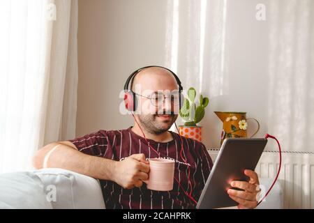 les jeunes ont un bon moment à la maison. écouter de la musique, boire du café et du thé. Adolescent au repos qui court avec une tablette et un leptop dans les mains. Banque D'Images