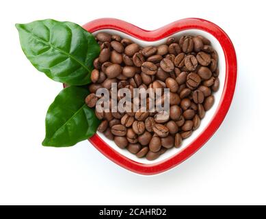 Grains de café dans un bol en forme de cœur isolé sur fond blanc. Arabica rôti avec feuilles vertes fraîches. Vue de dessus Banque D'Images